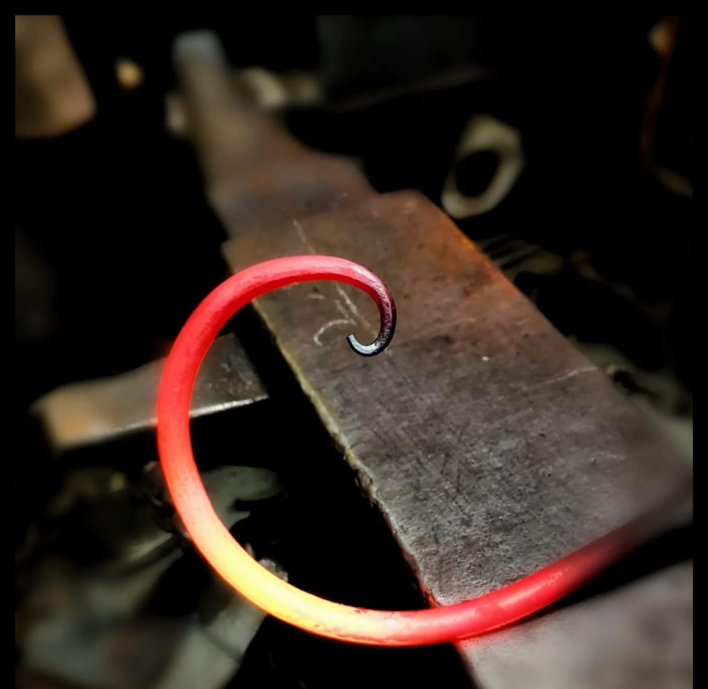 A length of steel curled into a scroll, still glowing red on the anvil