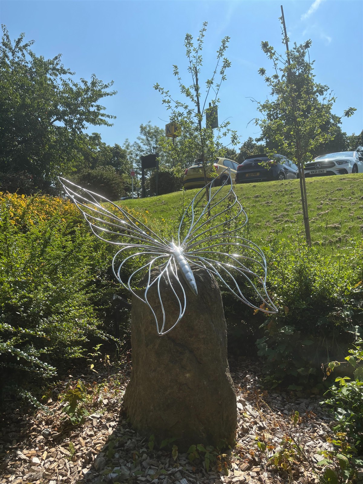 The Gift of Life butterfly in polished wire, resting on a standing stone in the sun